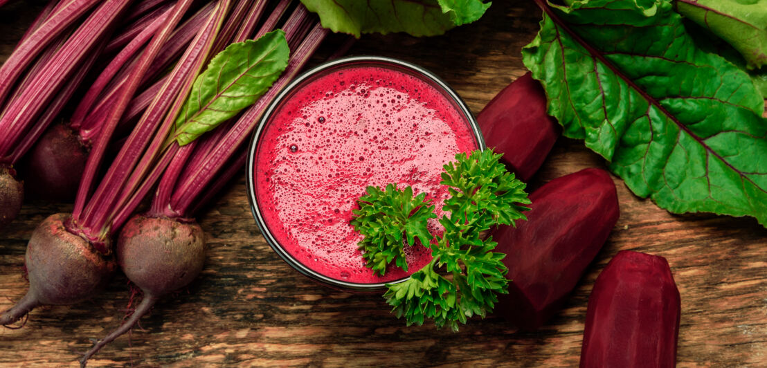 Rote-Bete-Smoothie und geschälte Rote-Bete-Knollen auf einem Holzuntergrund.