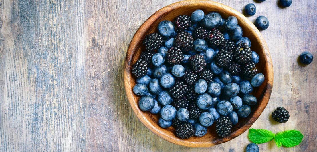 Heidelbeeren und Brombeeren in einer Holzschale.