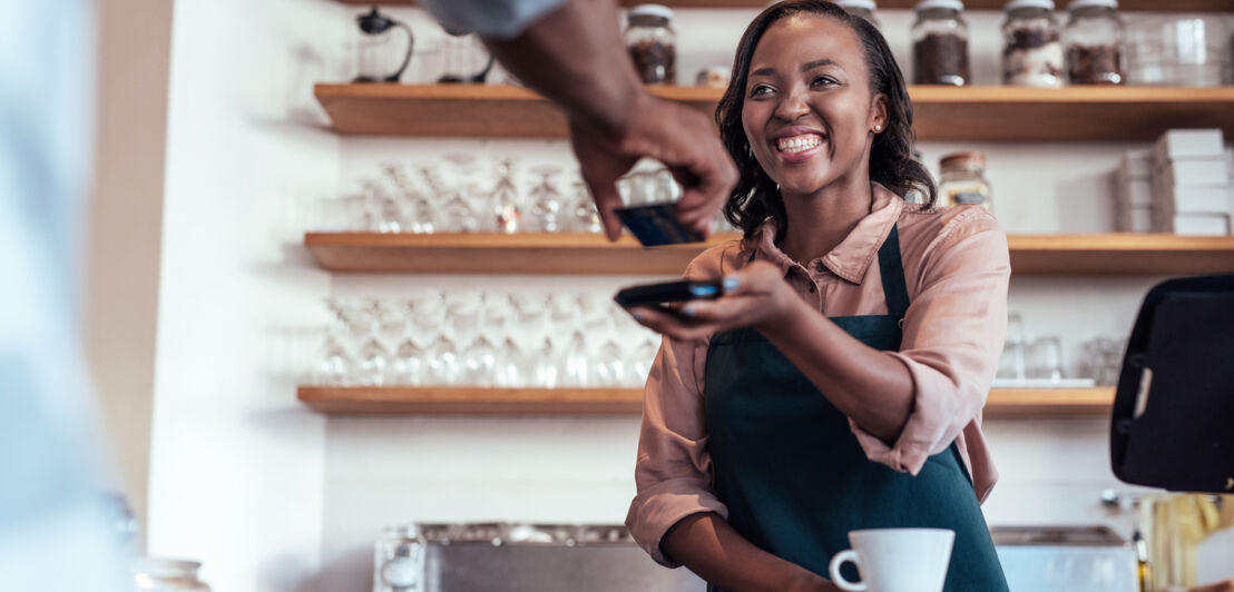 Eine lächelnde Barista reicht einem Gast ein Kreditkartenlesegerät