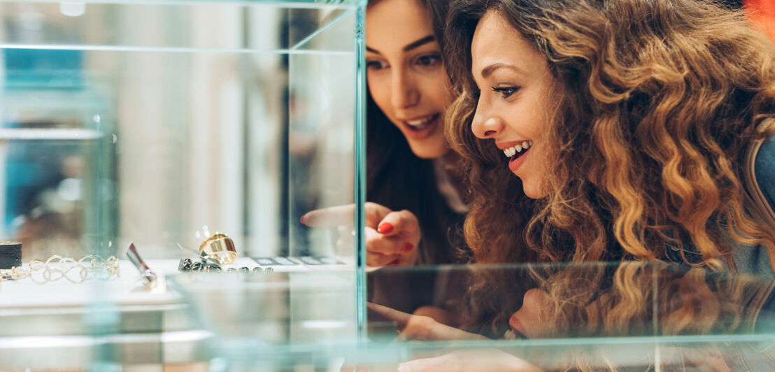 Nahaufnahme von zwei jungen Frauen, die auf Schmuckstücke in einer Vitrine in einer Boutique zeigen