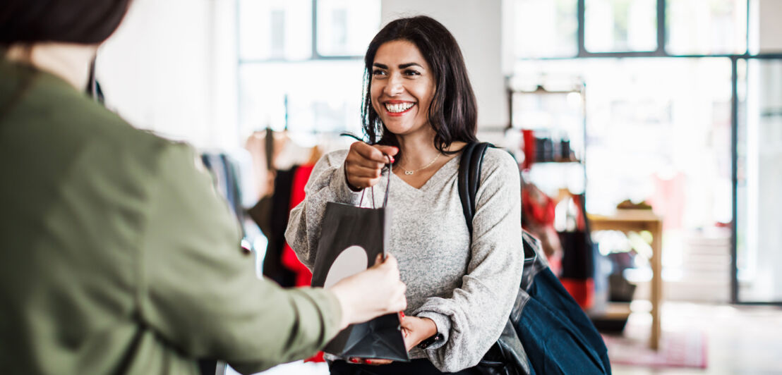 Eine Frau nimmt in einer Boutique lachend eine Tüte entgegen