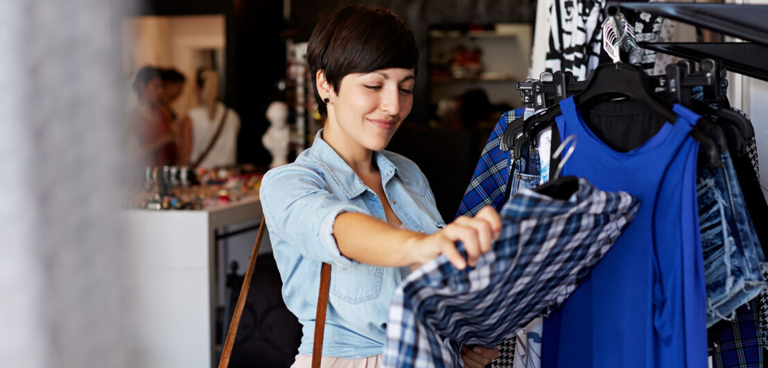 Eine junge Frau schaut sich in einer Boutique ein blaues Kleid an