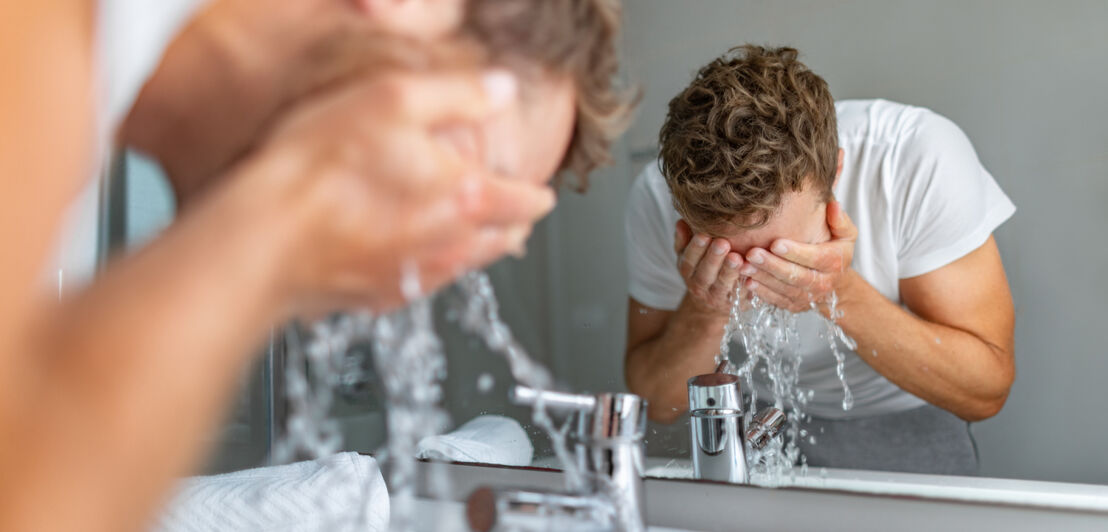 Ein junger Mann spritzt sich Wasser ins Gesicht.