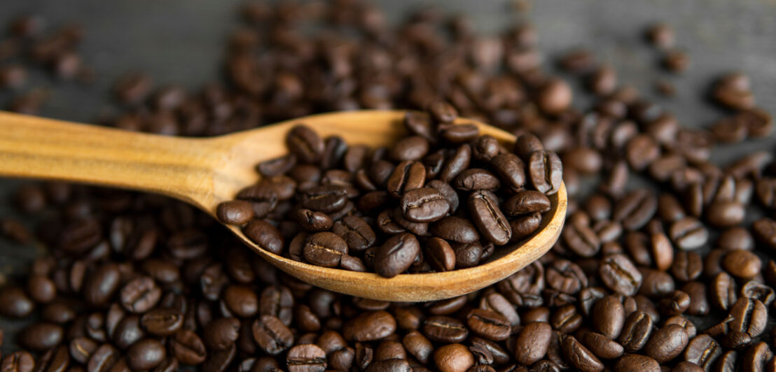 Kaffeebohnen und ein Holzlöffel, der mit Bohnen gefüllt ist