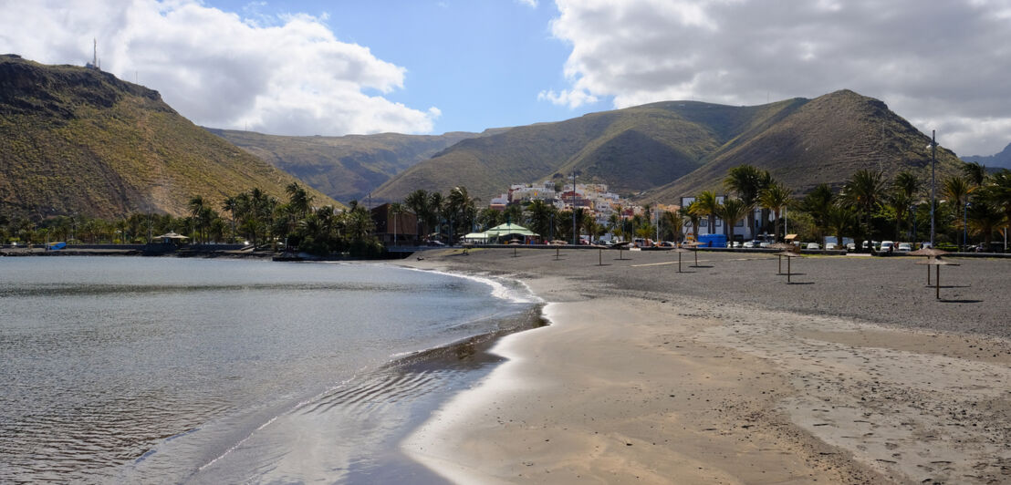 Sandstrand mit flachem Einstieg und Bergen im Hintergrund.