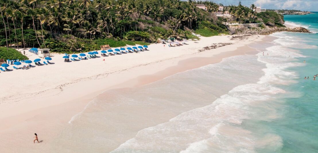 Sonnenliegen am weißen Sandstrand mit türkisblauem Wasser, ein Hotel im Hintergrund.