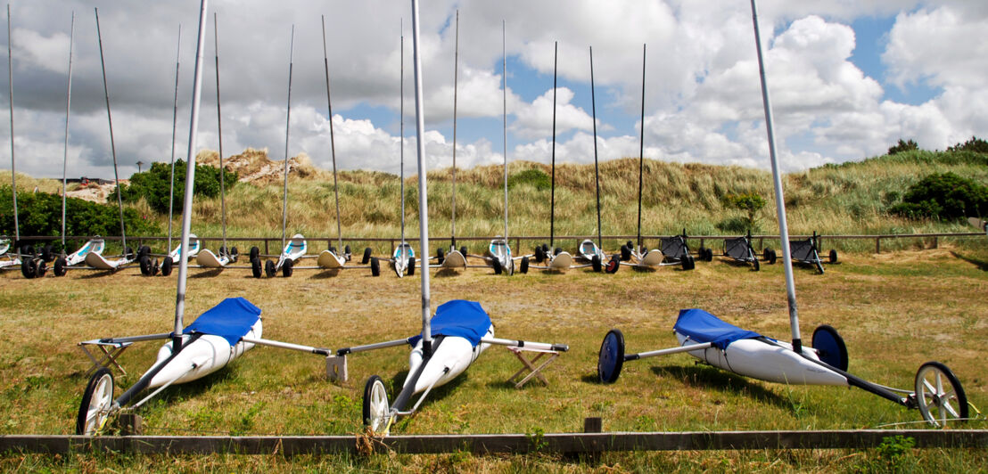 Mehrere Strandsegler parken vor einer Düne.