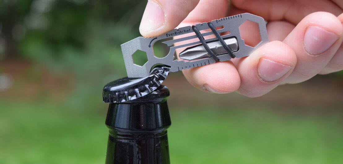 Mit einem Multitool wird eine Flasche mit Kronkorken geöffnet.