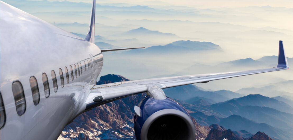 Luftaufnahme eines fliegenden Flugzeuges über einer wolkenverhangenen Gebirgslandschaft