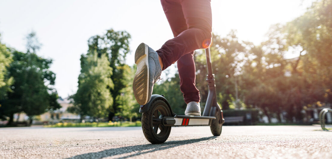 Eine Person fährt auf einem E-Scooter durch einen Park