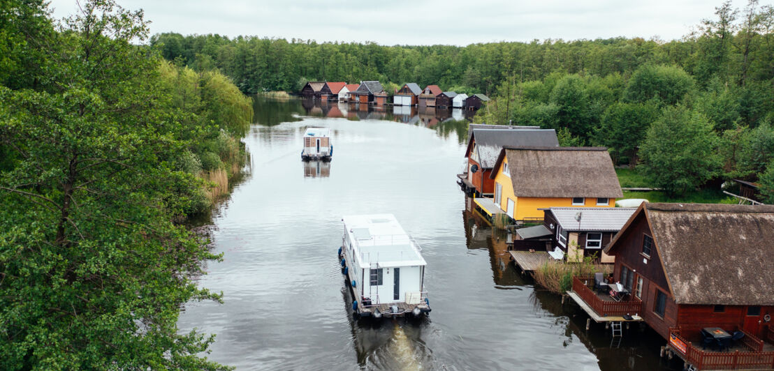 Hausboote schippern übers Wasser, am Rand stehen kleine Hütten