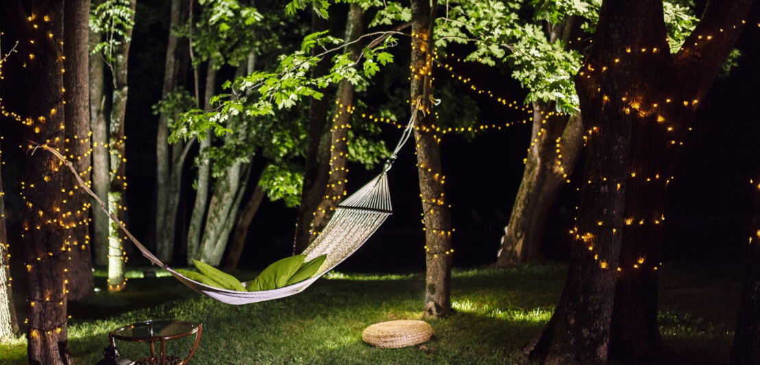 Eine Hängematte in einem Garten mit beleuchteten Bäumen bei Nacht