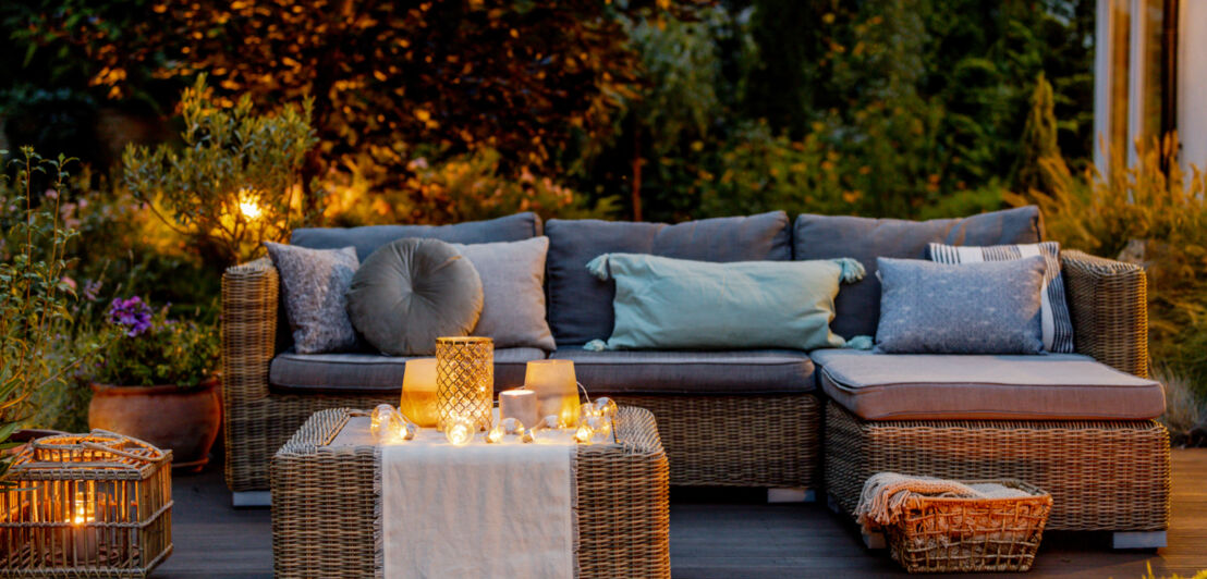 Ein Sofa auf einer Terrasse, dekoriert mit brennenden Kerzen und Windlichtern in der Abenddämmerung