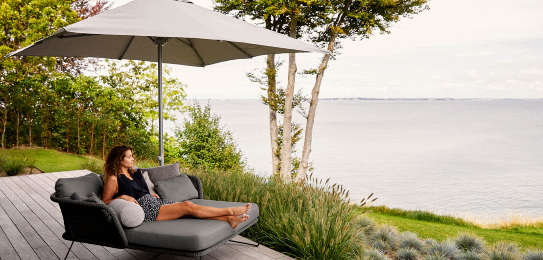 Eine Frau sitzt auf dem Gartenbett Horizon und blickt aufs Meer