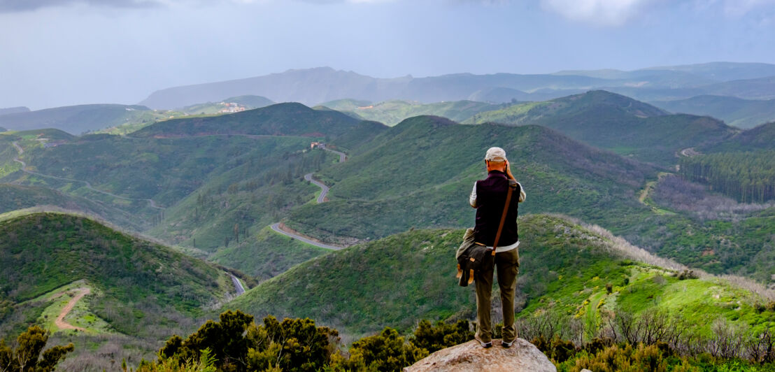 Ein Mann steht oben auf einem Berg und fotografiert ins Tal herunter