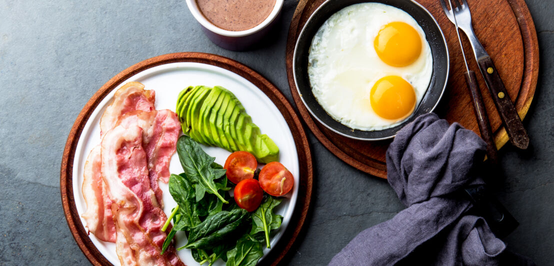 Zwei Teller mit Speck, Eiern, Salat und dazu eine Tasse Kaffee