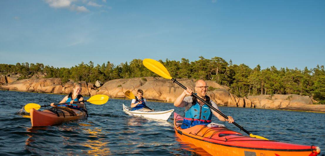 Eine Familie in Kajaks auf dem Wasser, im Hintergrund eine felsige Küste