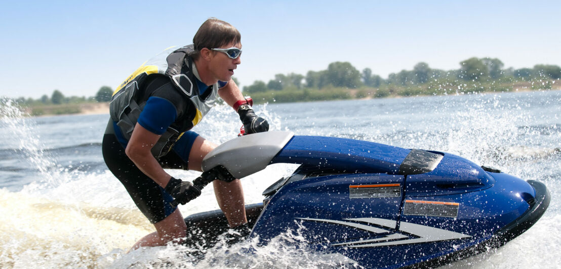 Ein Mann fährt in Neoprenanzug, Schwimmweste und Brille einen Jetski