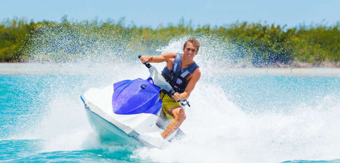 Ein junger Mann fährt rasant auf einem Jetski, hinter ihm die Gischt