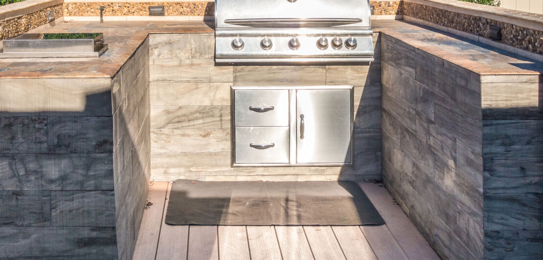 Eine Outdoorküche in Holzoptik mit einem integrierten Gasgrill.