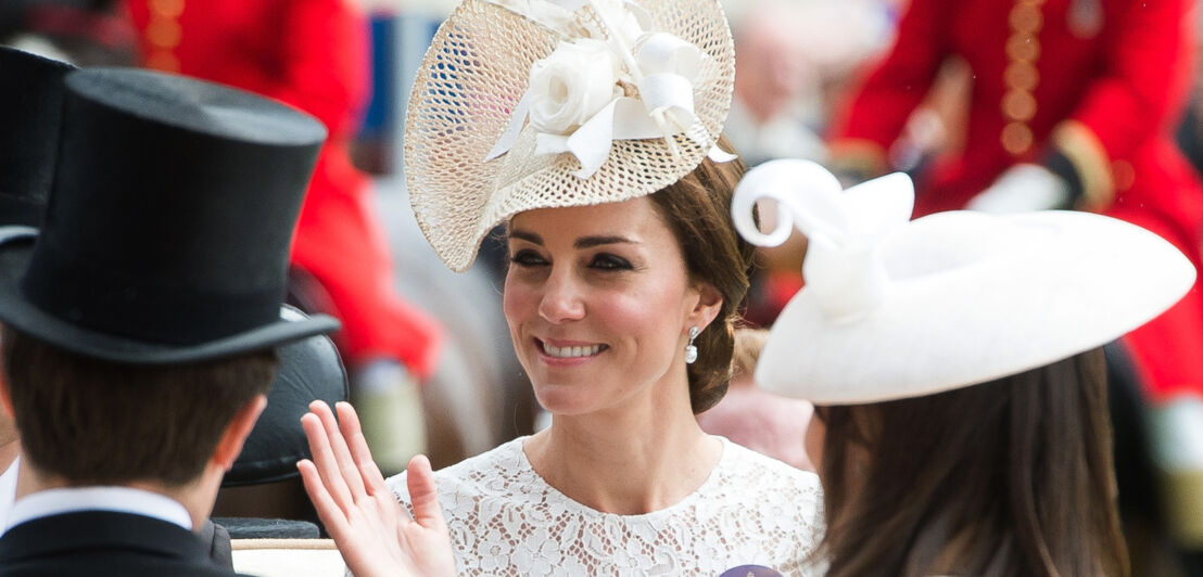 Nahaufnahme von Herzogin Catherine, die mit einem eleganten, weißen Fascinator auf dem Kopf aus einer Kutsche winkt