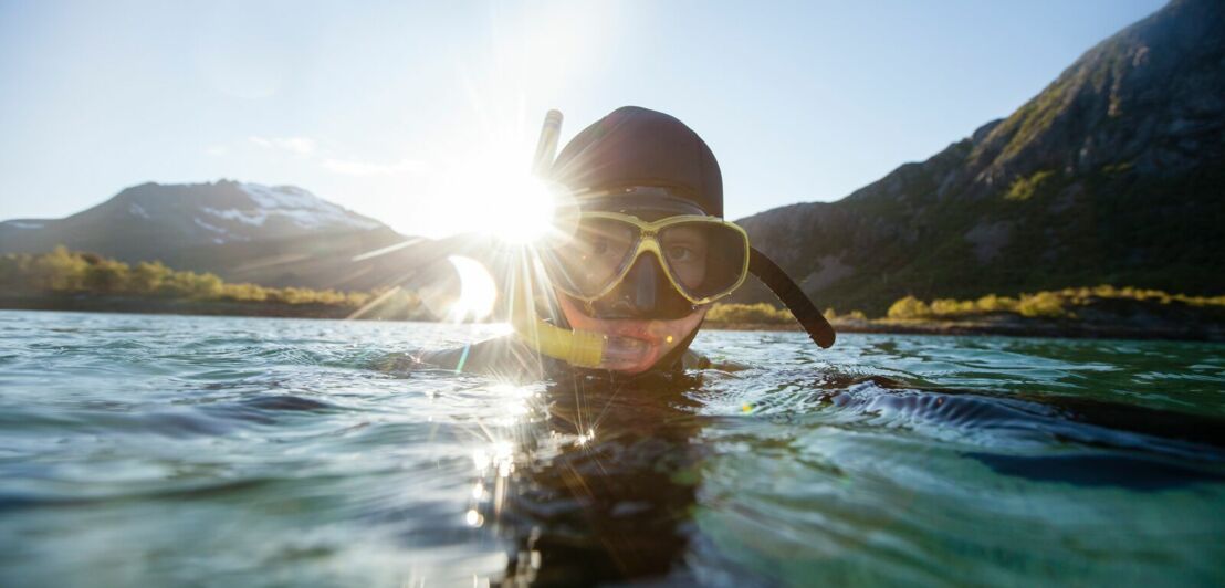 Ein Taucher mit Taucherbrille und Schnorchel taucht aus dem Wasser auf