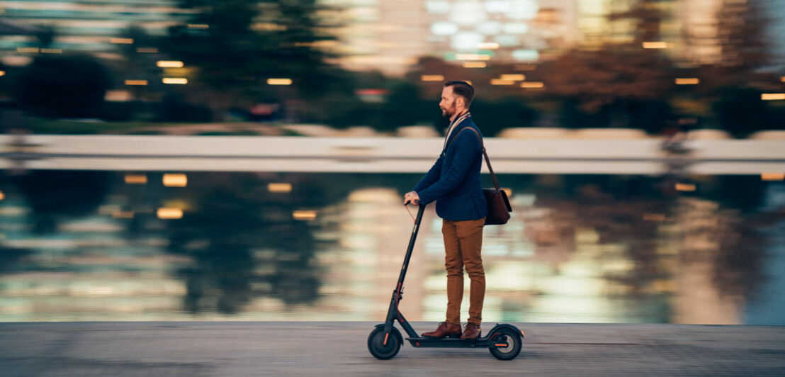 Profilansicht eines Geschäftsmannes, der auf dem Weg zur Arbeit einen Roller fährt