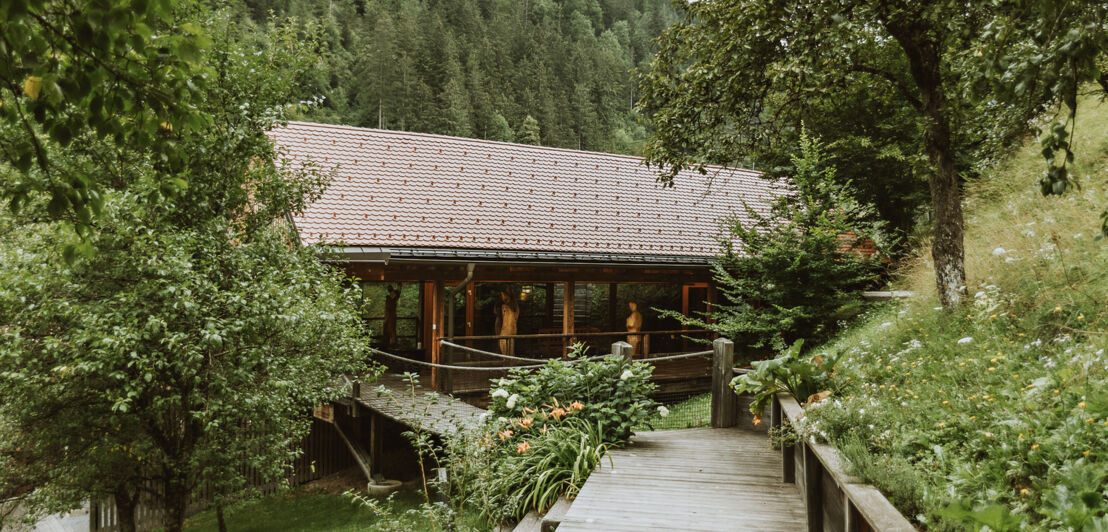 Ein Haus mitten im Grünen, zu dem ein Holzsteg führt.