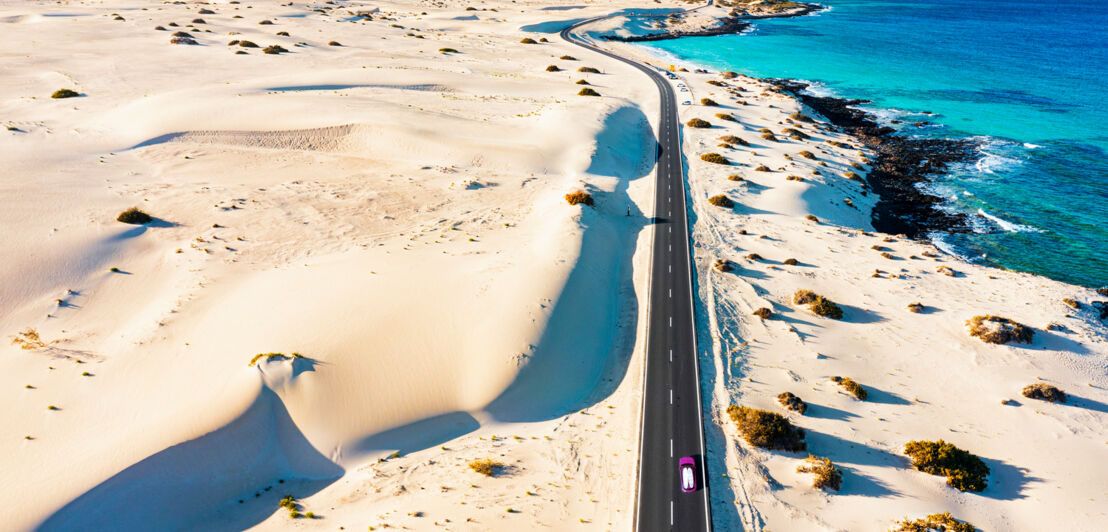 Landschaft mit Sanddünen am Meer, durch die eine Küstenstraße führt