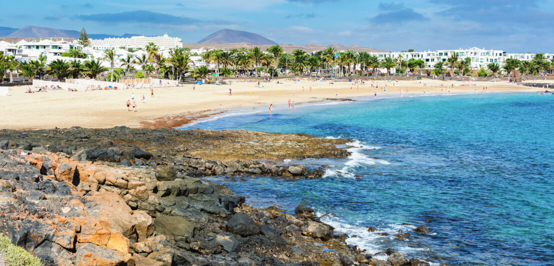 Belebte Bucht mit Sandstrand, Hotels und Palmen