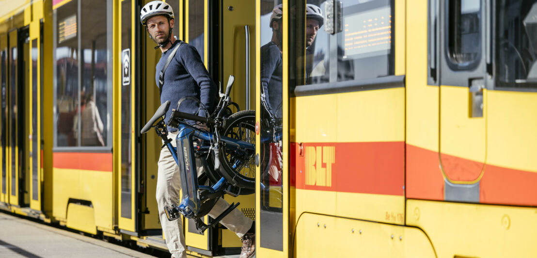 Ein Mann steigt mit einem Klapprad aus einer Tram