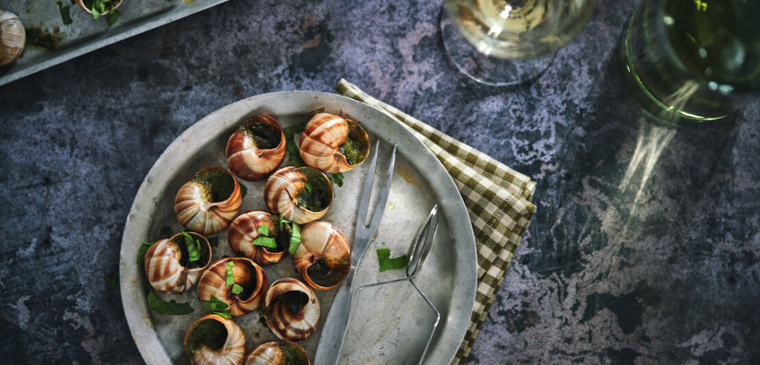 Ein Metallteller mit Schnecken, Schneckengabel, Schneckenzange und Weißwein