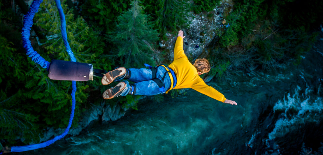 Ein Mann springt am Bungeeseil in die Tiefe, unter ihm fließt ein Fluss.