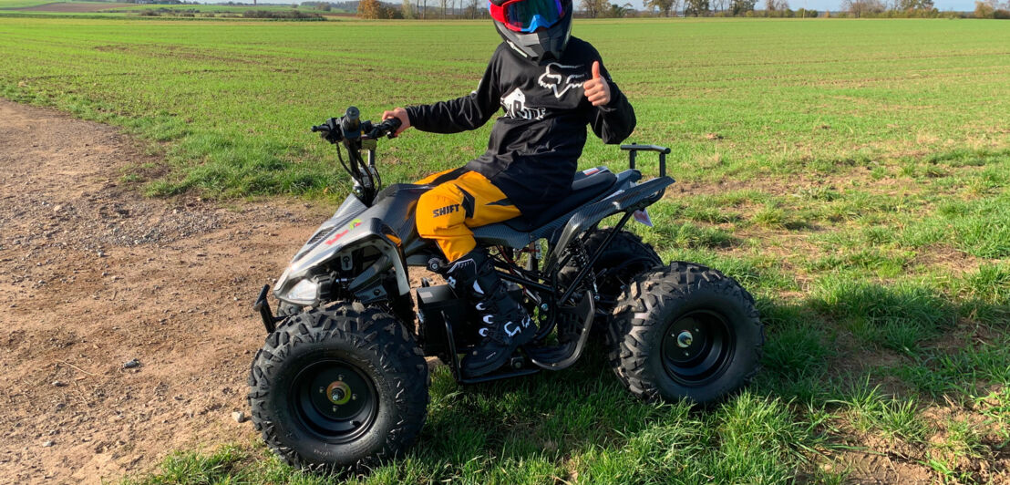 Ein Junge sitzt auf einem Quad, das auf einer Wiese steht. TR300