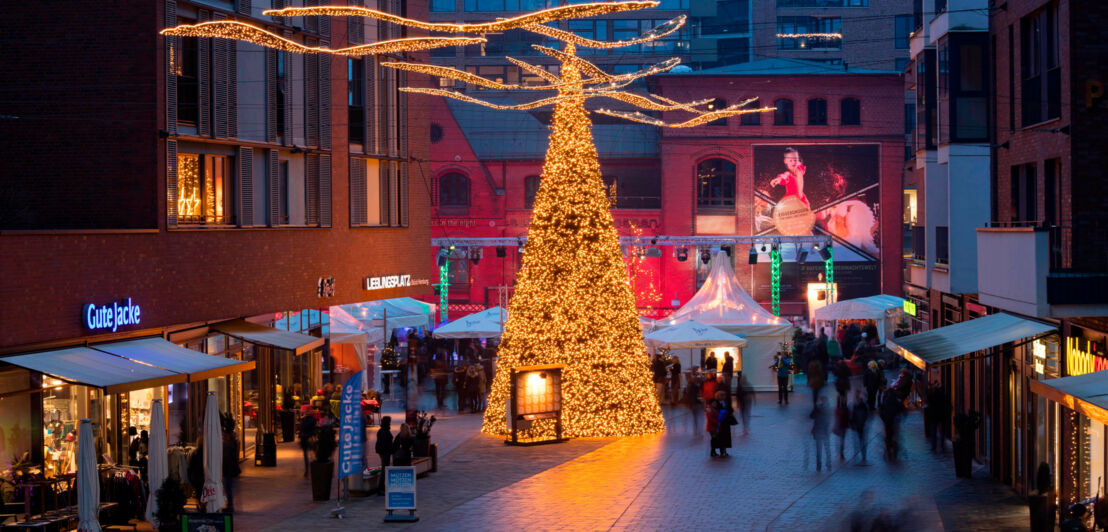 Erleuchteter Weihnachtsbaum mit Marktständen zwischen modernen Gebäuden in einer Einkaufsstraße