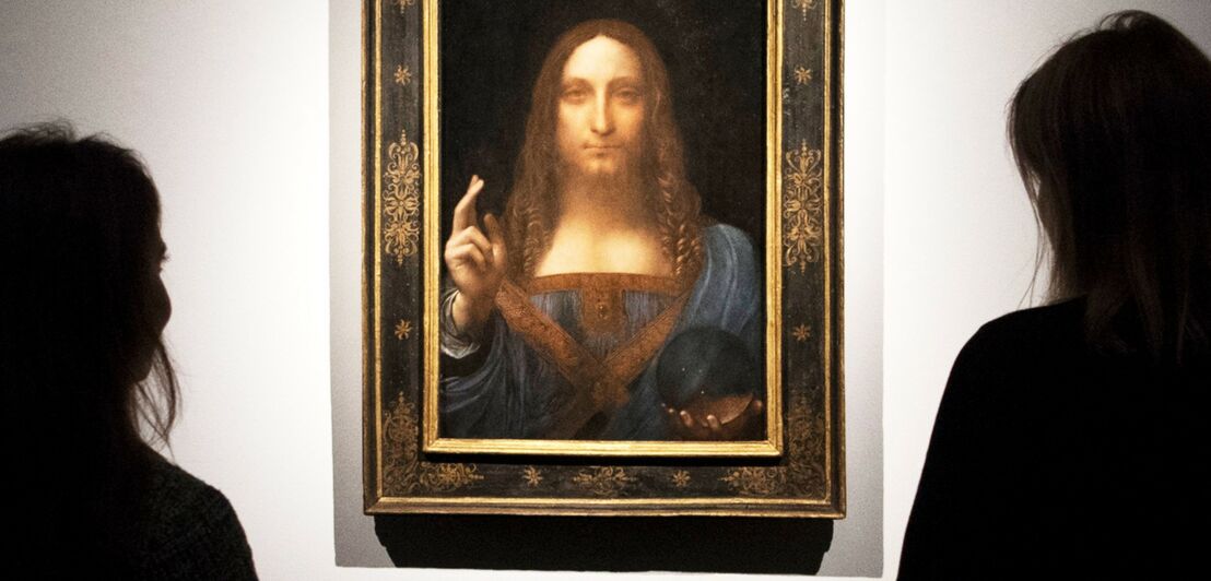 Das Gemälde Salvator Mundi an einer Wand, davor zwei Betrachterinnen im Anschnitt