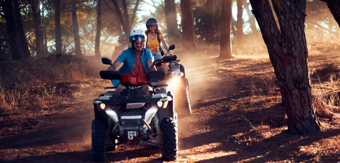 Ein Paar fährt auf zwei Quads gut gelaunt durch einen Wald