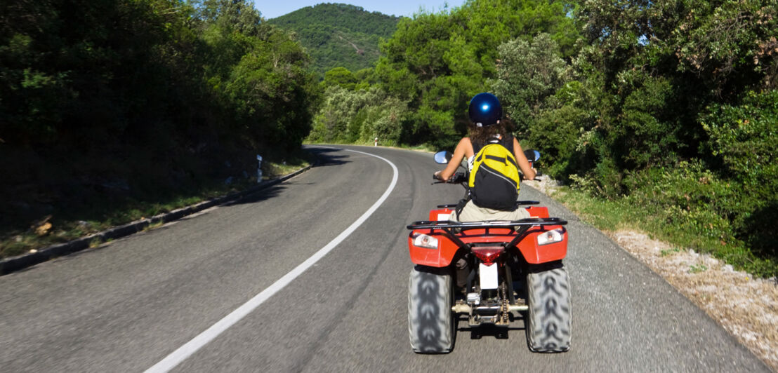 Eine Frau in sommerlicher Kleidung fährt auf einem Quad eine Straße entlang