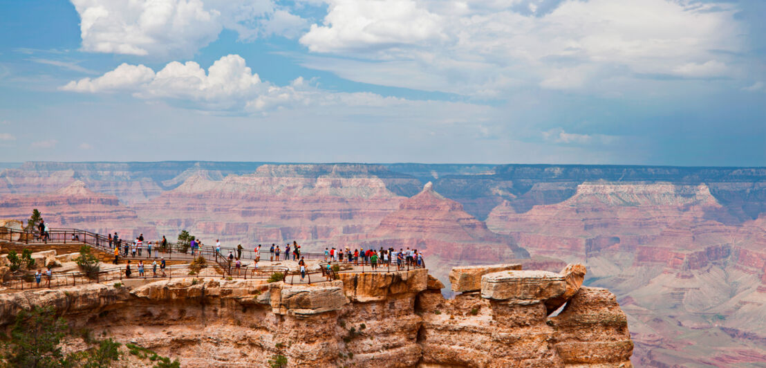 Viele Menschen stehen im Yellowstone-Nationalpark auf einem Felsen und blicken über die Schluchten und Felsformationen, die sich vor ihnen erstrecken.