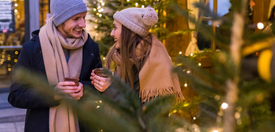 SYMBOLBILD Junges Paar trinkt ein Heißgetränk auf dem Weihnachtsmarkt.