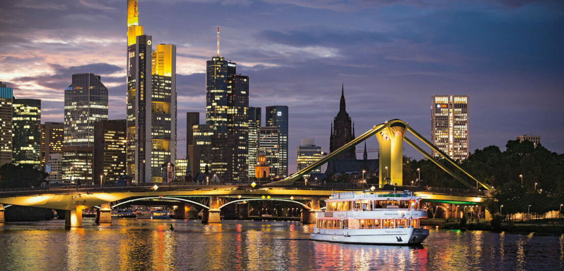 Personenschiff auf dem Main vor der Frankfurter Skyline in der Abenddämmerung.