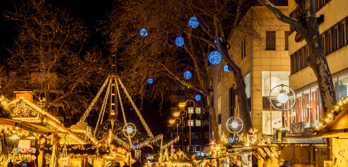 Beleuchtete Buden in einer Einkaufsmeile, an den Bäumen hängen blaue Lichtkugeln