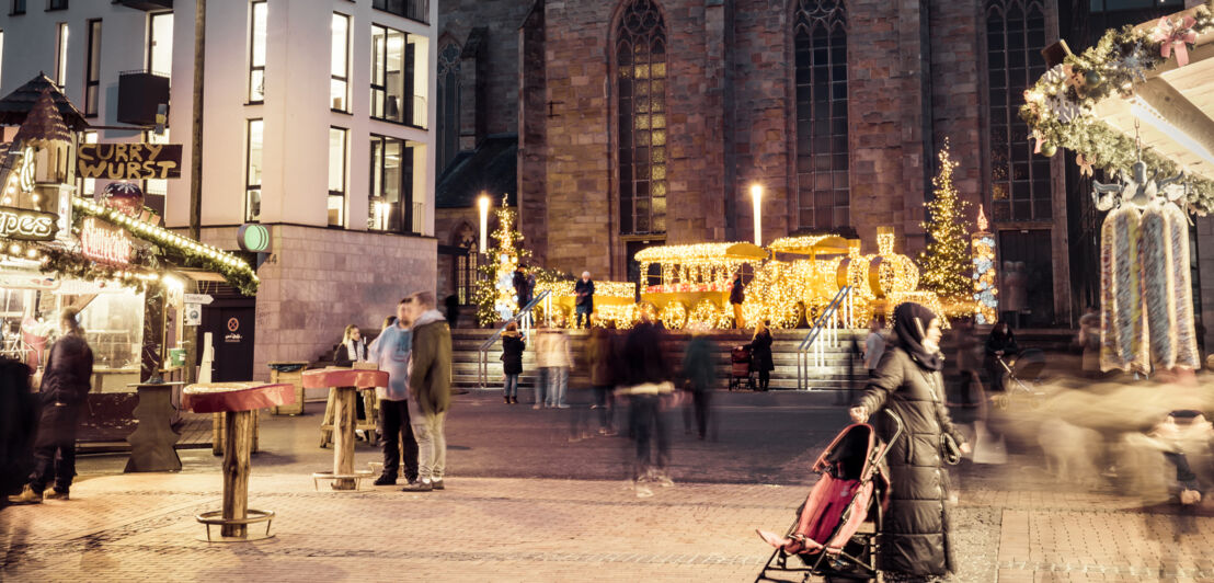 Blick auf eine Lichtinstallation in Zugform, vorbei an Weihnachtsmarktständen