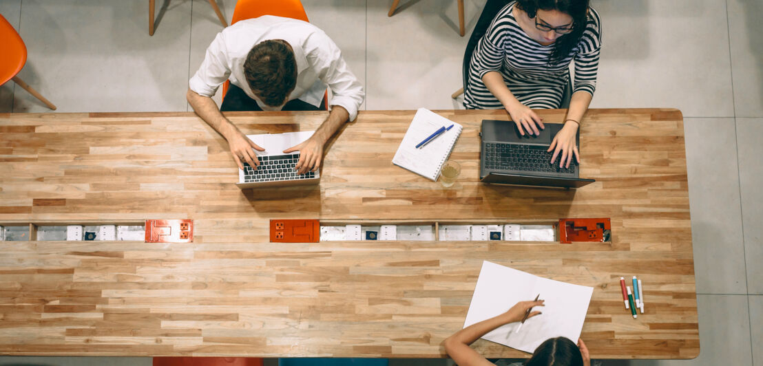 Mehrere Personen sitzen an einem Tisch mit Laptops und arbeiten