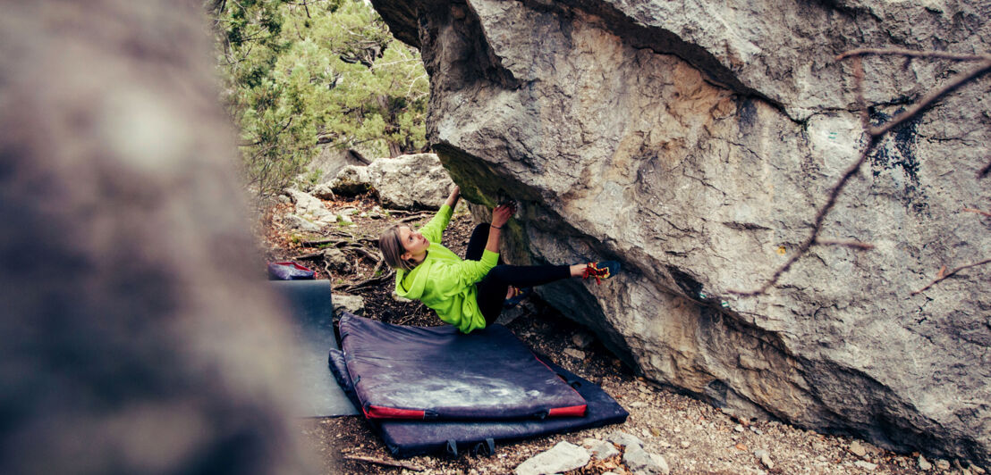 Eine Person bouldert an einer Felswand, unter ihr liegt eine weiche Matte.