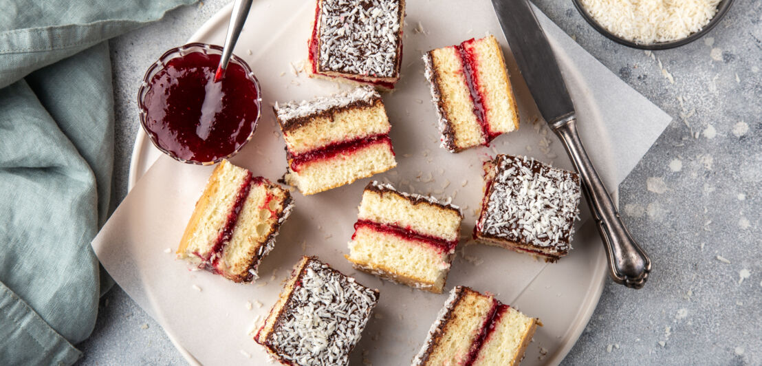 Kuchenwürfel mit Schokoglasur, Kokosraspeln und Marmeladenfüllung auf einem Teller