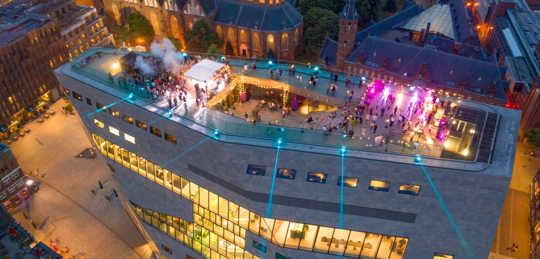 Luftaufnahme einer Veranstaltung auf einer großen Dachterrasse eines modernen, städtischen Gebäudekomplexes bei Nacht