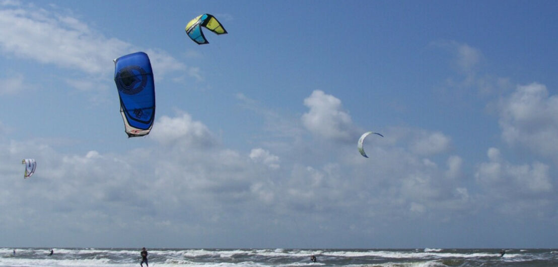 Kiteboarder gleiten am Strand von Juist durch die Wellen.