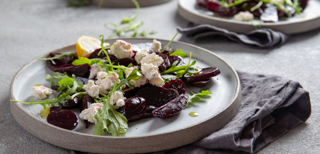 Rote-Bete-Käse-Salat Carpaccio mit Rucola und Zitrone, serviert auf einem hellen Teller, darunter liegt eine dunkle Stoffserviette