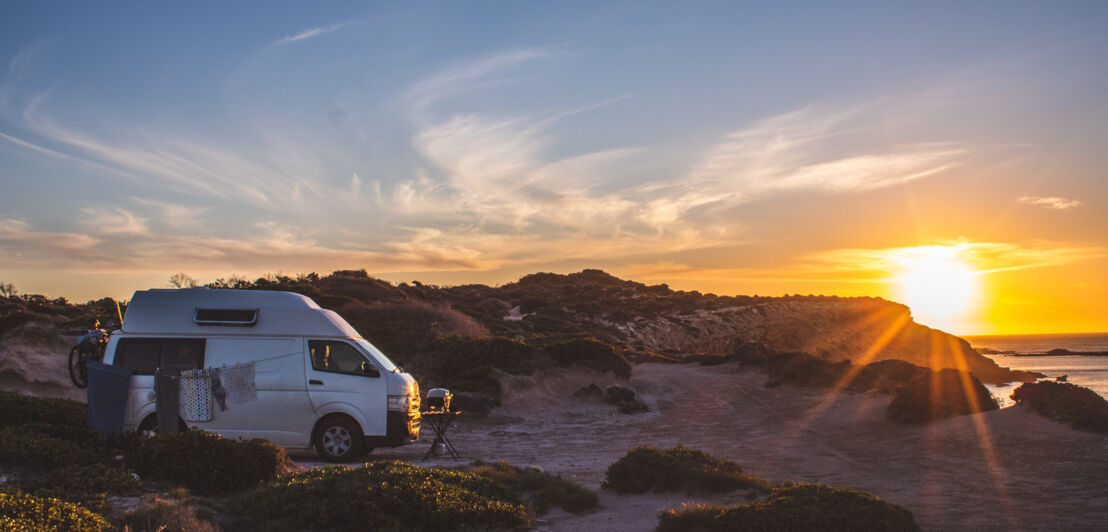 Ein Camper an einer Klippe am Meer bei Sonnenuntergang